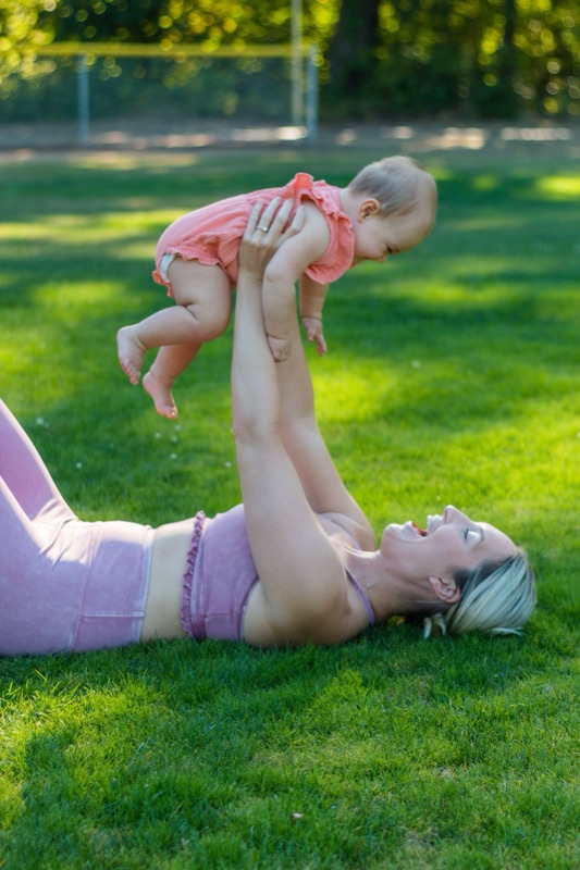 A parent playfully lifting their baby overhead outdoors, both smiling